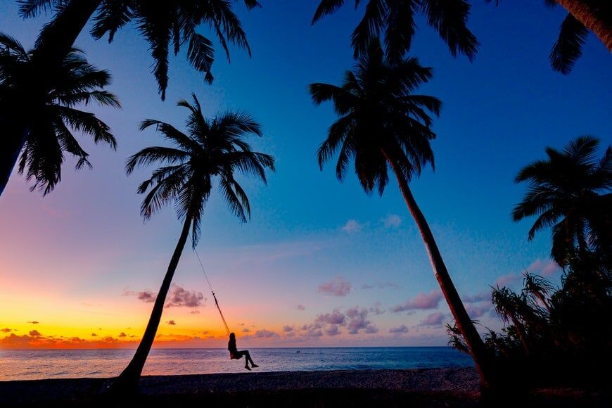 Silhouet van meisje op een schommel met palmbomen