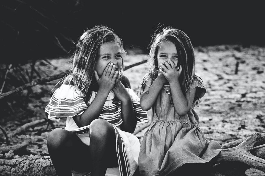 Fotoshoot ideeën- twee jonge meisjes zitten en lachen in zwart-wit