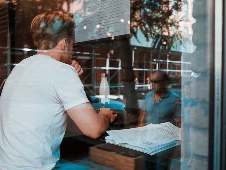Man die in een café zit te werken met een reflectie van mensen buiten op het raam
