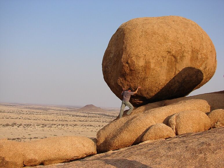 Sisyphus-achtige man duwt rotsblok bergopwaarts 