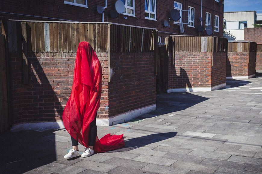 Afbeelding van persoon gedrapeerd in rode stof die in stedelijke omgeving loopt