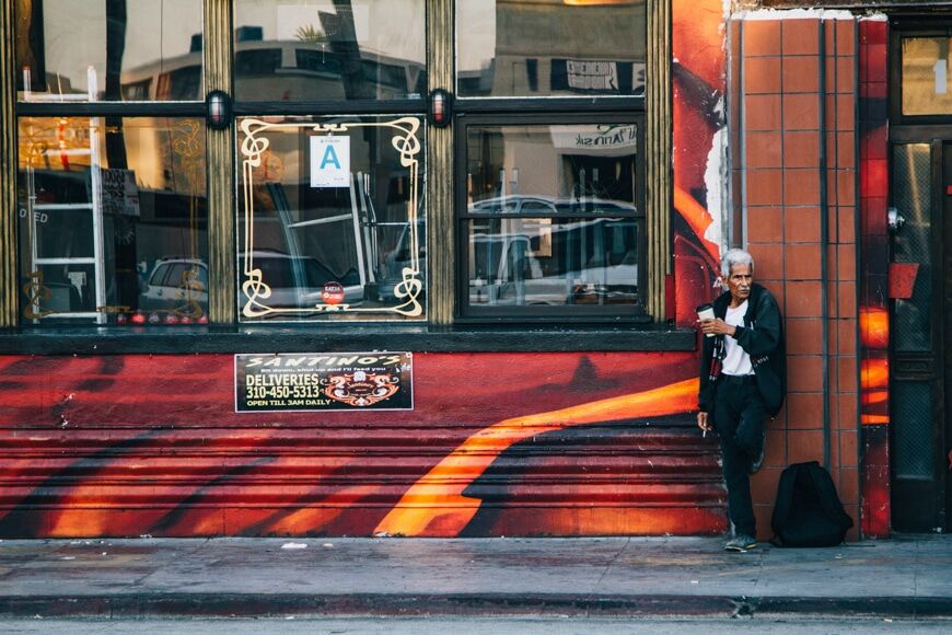 Fotografie in de stad - oudere man leunend tegen een winkelpui met een koffie