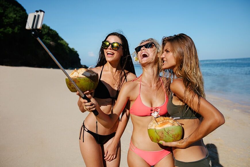 Groep gelukkige jonge vrouw met kokosnoten die selfie maakt op het strand. Drie jonge vrouwen in bikini op de zee shire maken zelfportret met smartphone.