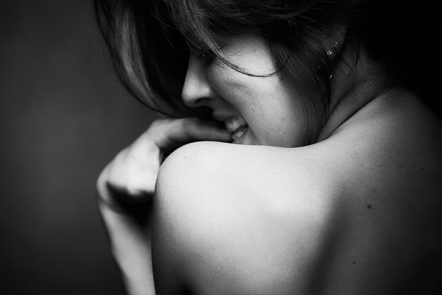 Zwart-witfoto van een naakte rug van een vrouw die in haar vingers bijt