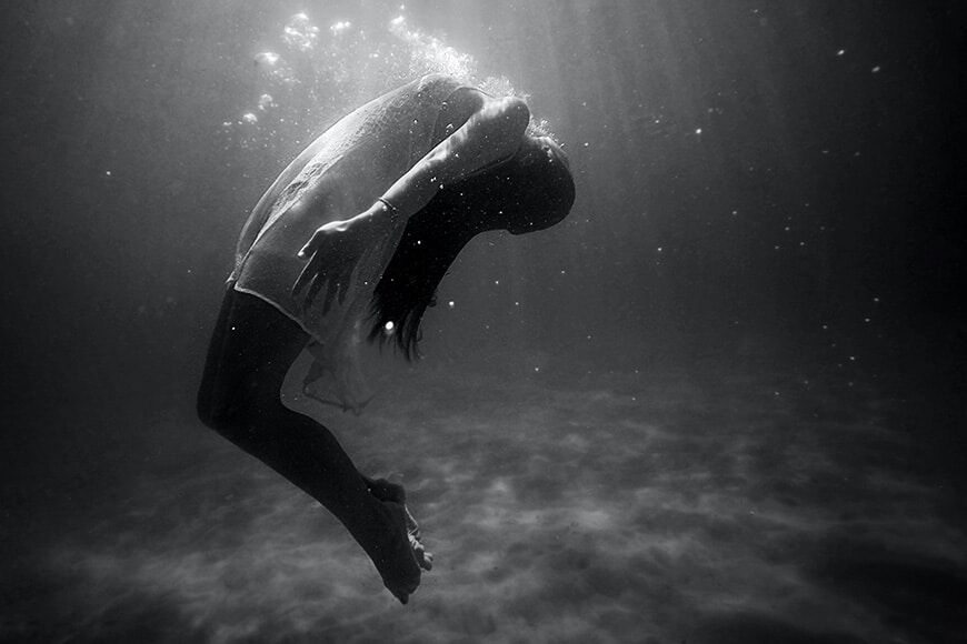 Zwart-witfoto van een vrouw onder water die naar achteren buigt