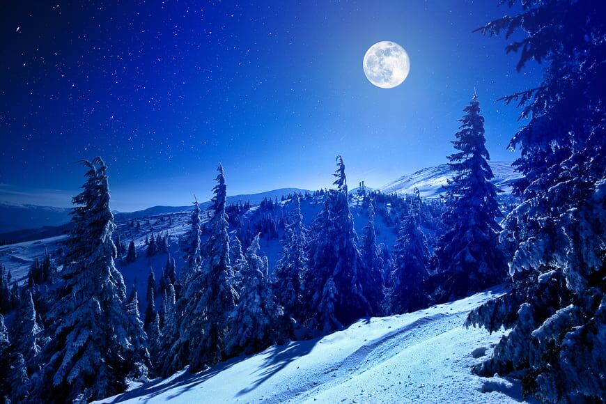 Maan en sterren boven besneeuwde bergen.