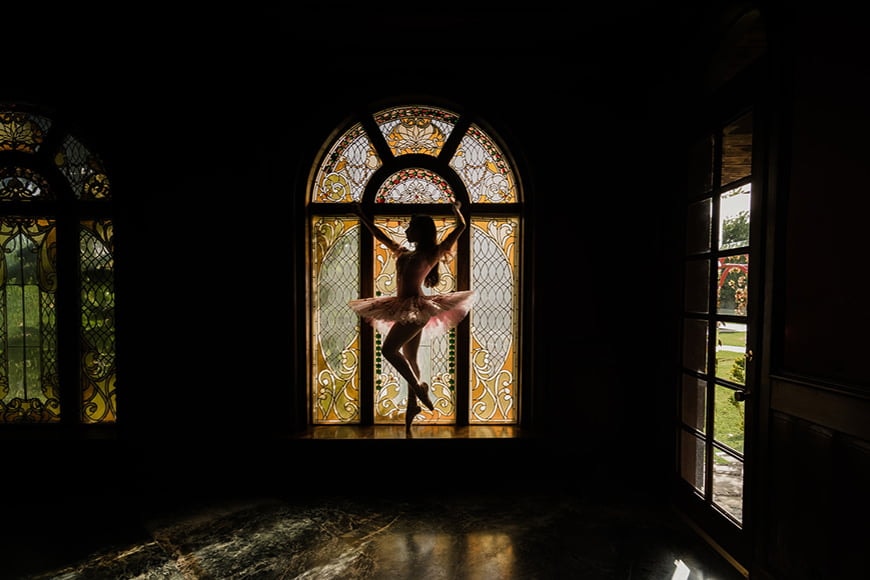 Ballerina silhouet tegen een glas-in-loodraam.