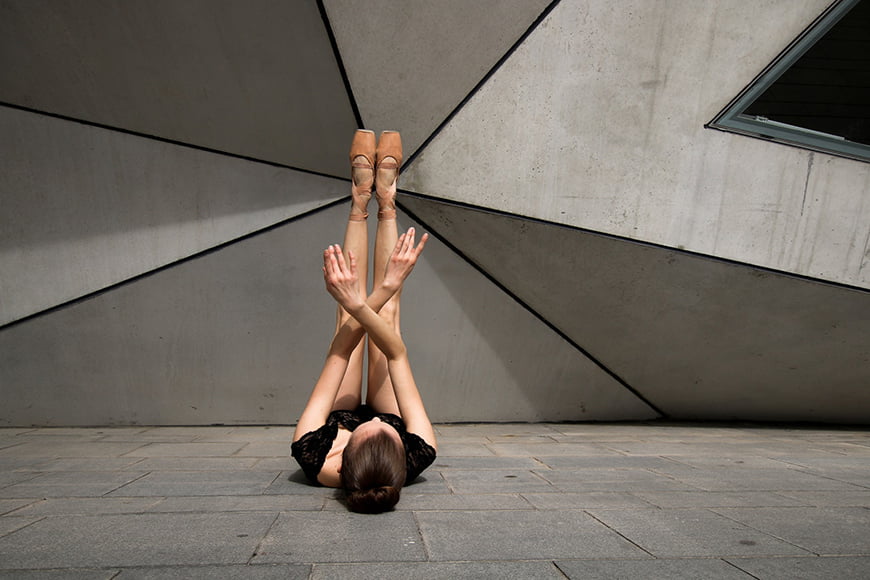 Balletmodel poseert tegen moderne architectuurachtergrond.