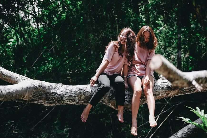 Twee lachende meisjes zittend op boomtak